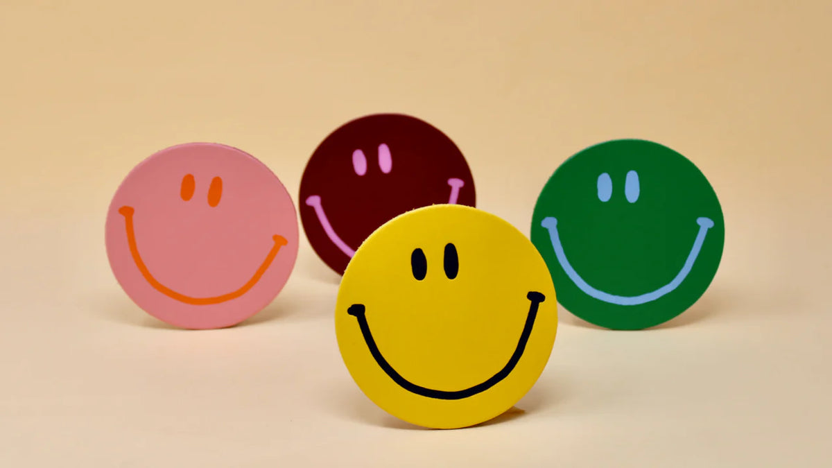 Four smiley leather coasters standing up in pink, red, green and yellow