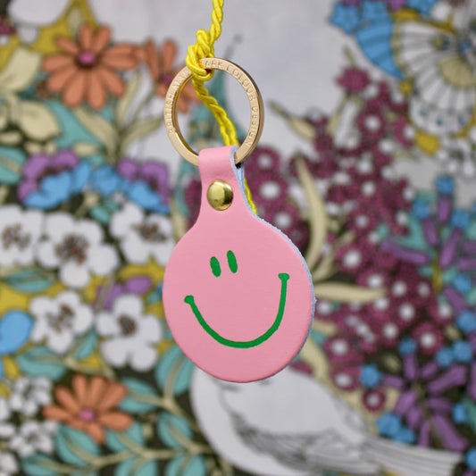 Ark pink leather smiley face key fob against a floral pattern