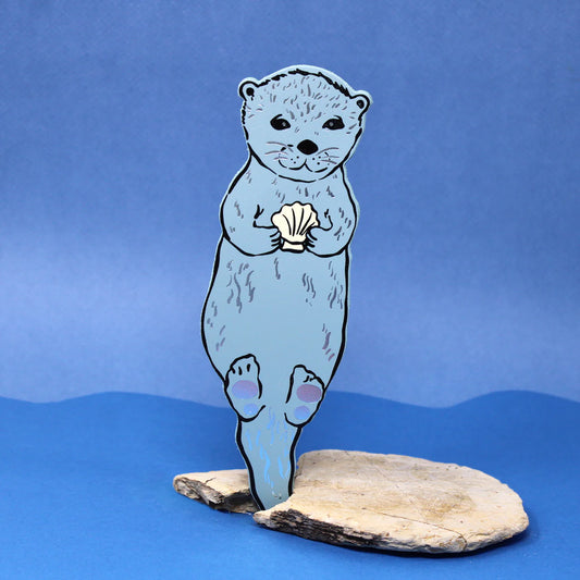 Ark blue grey otter bookmark holding a shell, standing on a rock