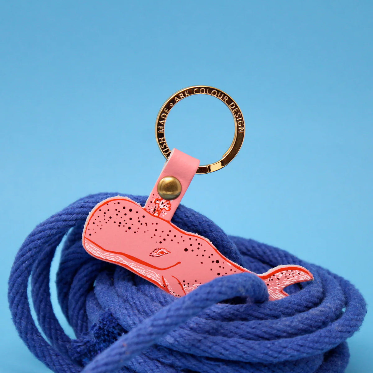 Pink leather humpback whale key fob on a gold ring, resting on blue rope