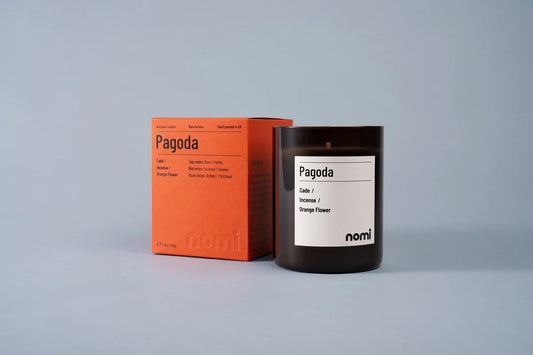 Nomi Pagoda scented candle in an amber jar beside its orange box