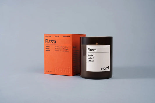 Nomi Piazza scented candle in an amber jar beside its orange box