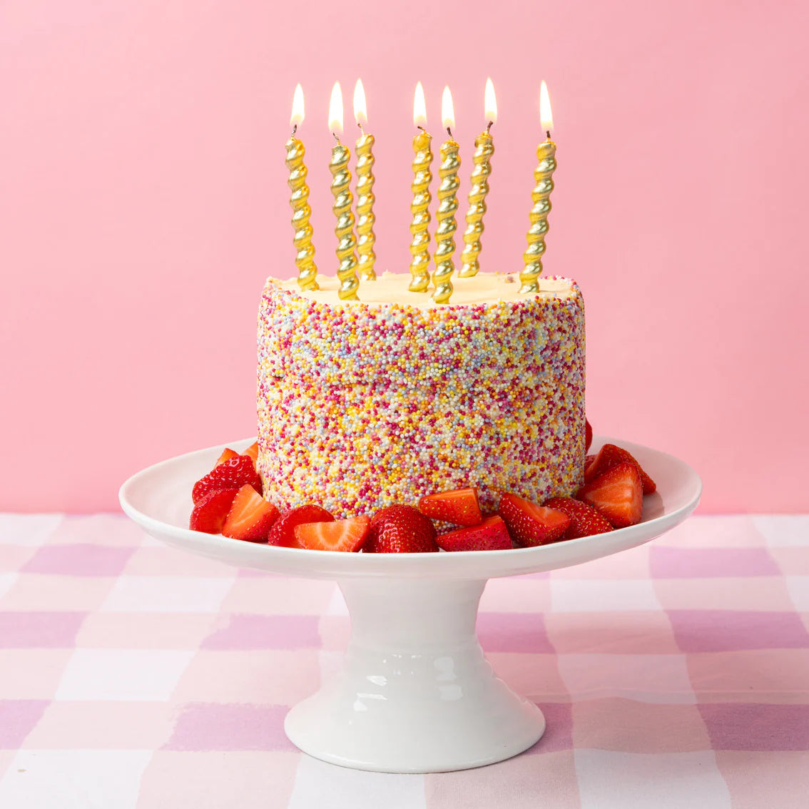 Sprinkle-covered birthday cake with lit gold twirl candles