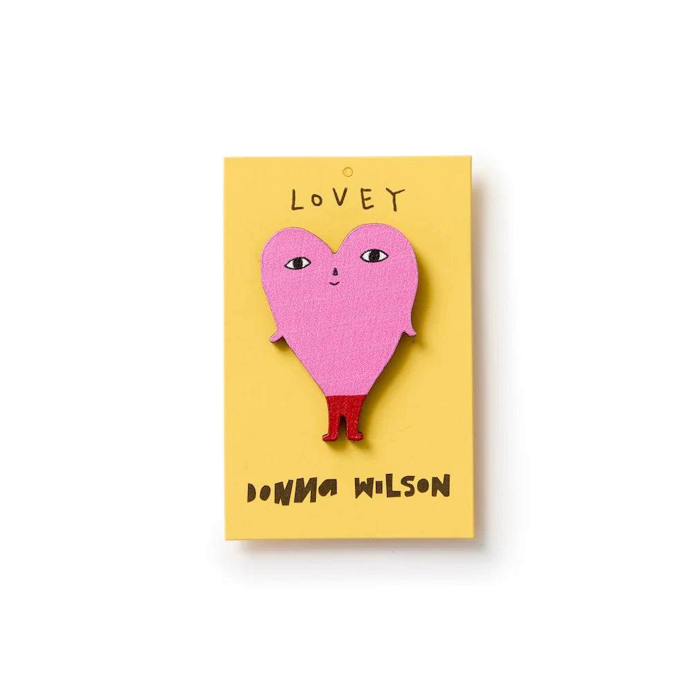 Donna Wilson Lovey pin badge: a pink heart with a face and legs, on its yellow card