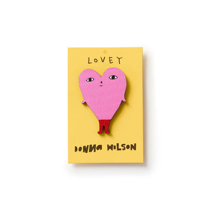 Donna Wilson Lovey pin badge: a pink heart with a face and legs, on its yellow card