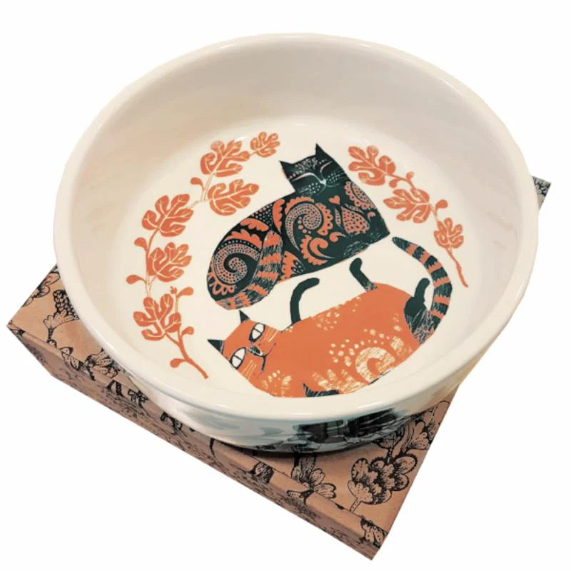 White ceramic cat bowl painted inside with a black and an orange patterned cat among orange leaves, on its gift box
