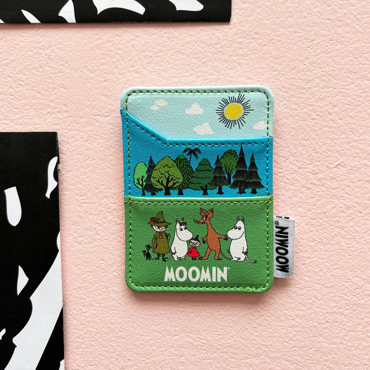 Moomin card holder: the Moomin family in a green landscape under blue sky, against pink
