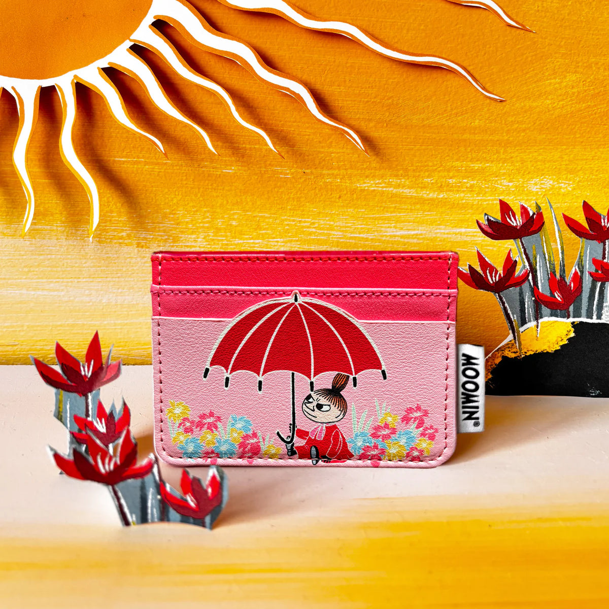 Pink Moomin Little My card holder with Little My under a red umbrella among flowers, in front of a painted desert scene