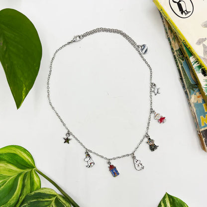 Silver chain necklace with enamel Moomin family charms, laid flat beside a leaf