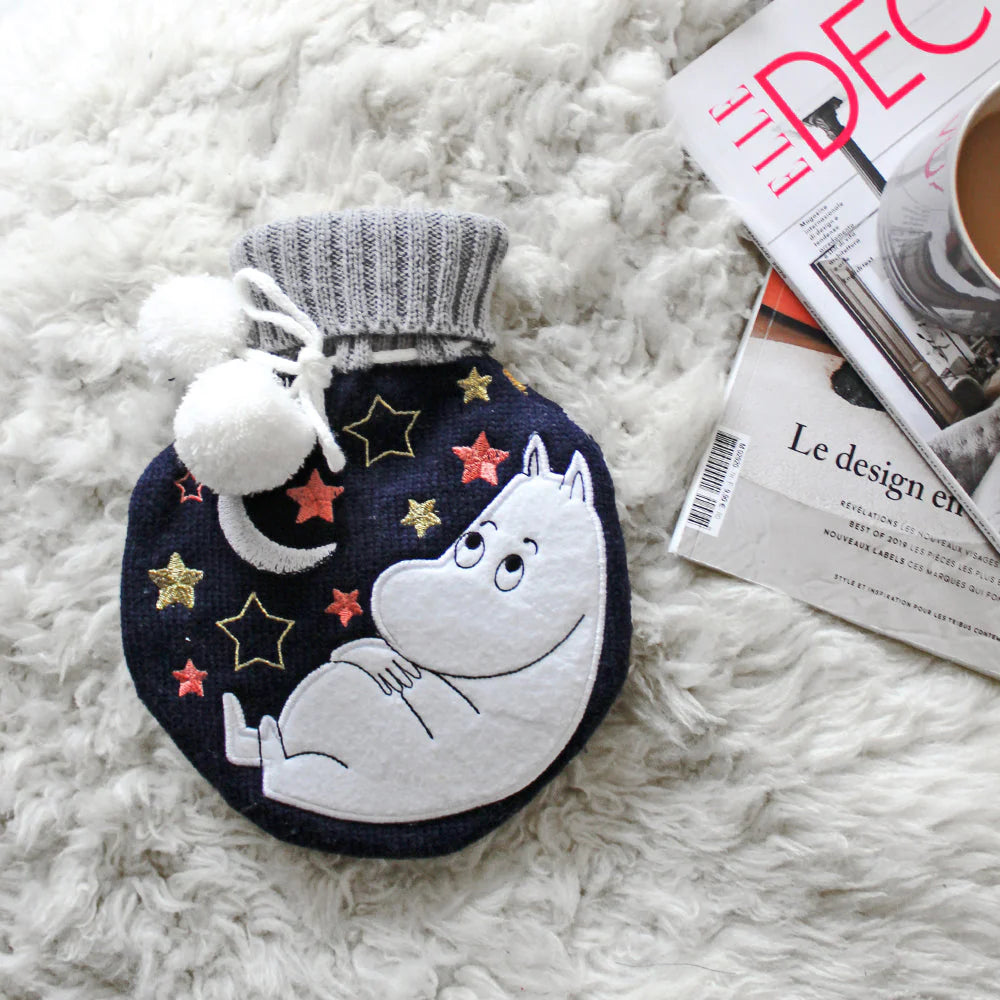 Moomin moon hot water bottle on a white sheepskin with magazines