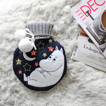 Moomin moon hot water bottle on a white sheepskin with magazines