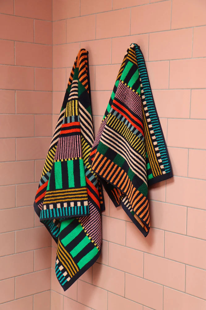 Two Donna Wilson striped towels hanging on a pink tiled wall