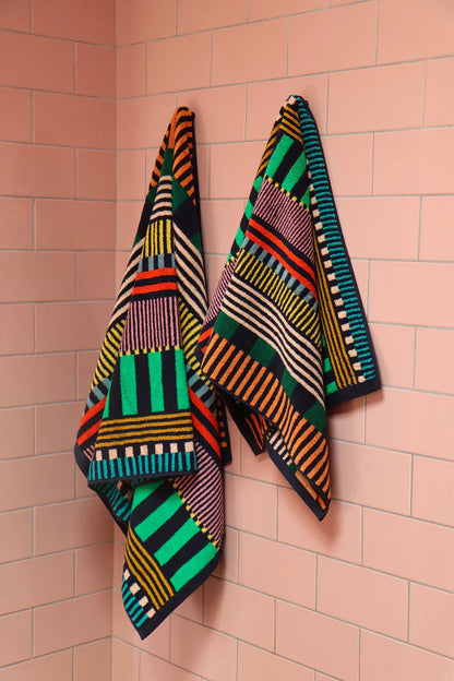 Two Donna Wilson striped towels hanging on a pink tiled wall