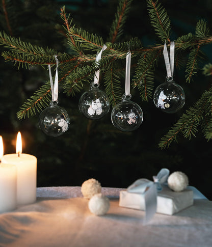 Moomin baubles hanging on a pine branch by candlelight