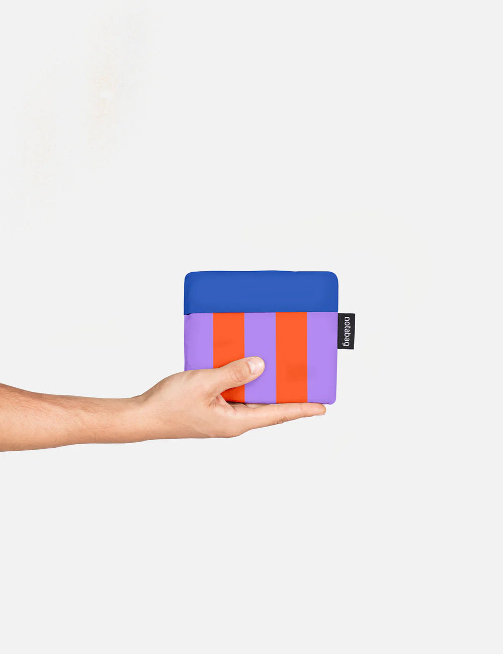 Hand holding the Notabag folded into its own small square pouch