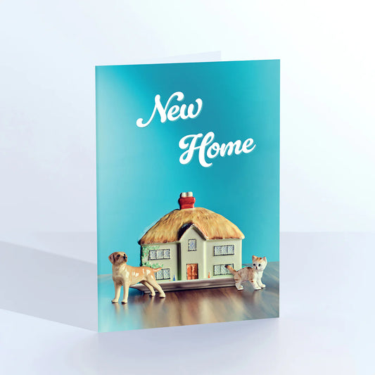 Ornament card: a thatched cottage figurine with two dogs, with 'New home' on teal
