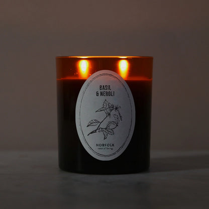 Basil & Neroli candle lit, with two flames glowing through the amber glass