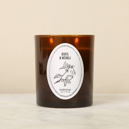 Norfolk Natural Living Basil & Neroli candle in an amber glass jar with an oval botanical label