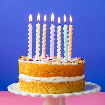 Sponge cake with lit pastel twirl candles against a blue background