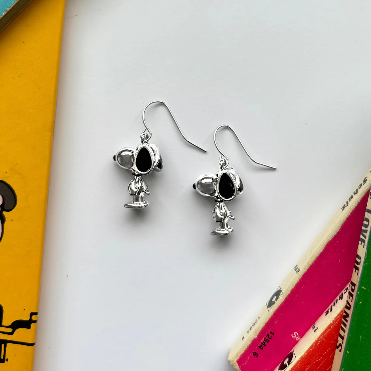 Silver Snoopy drop earrings on hooks, lying among Peanuts books