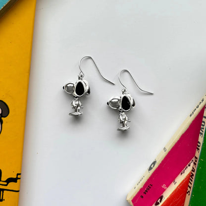 Silver Snoopy drop earrings on hooks, lying among Peanuts books