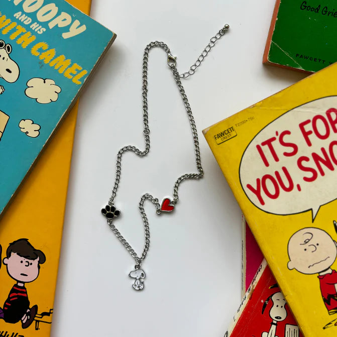 Peanuts Snoopy charm necklace with a red heart and paw print among Peanuts books