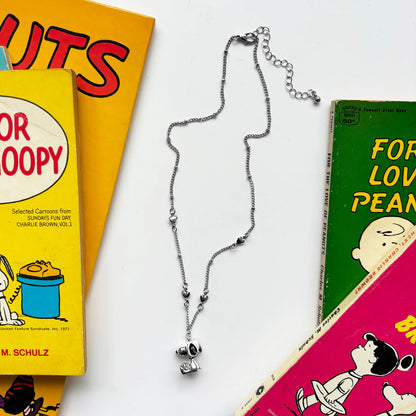 Silver chain necklace with a small 3D Snoopy charm, laid on Peanuts books