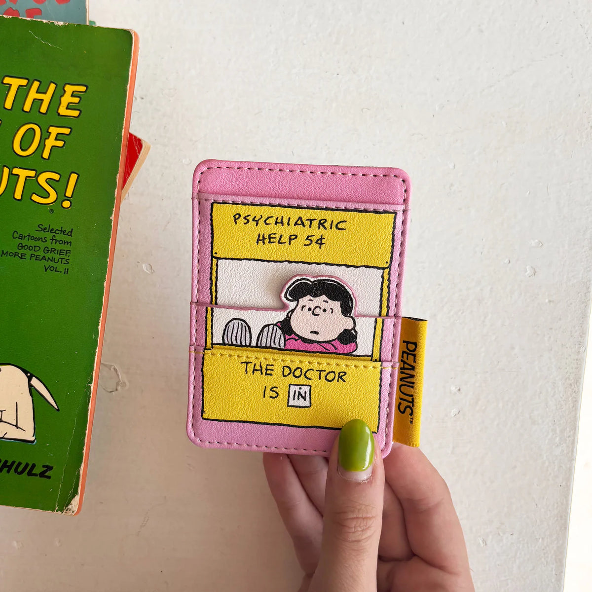 Hand holding the Lucy card holder next to a Peanuts comic book