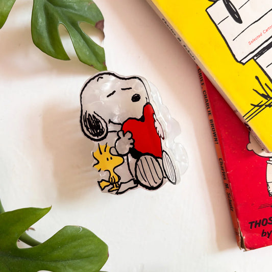 Clear Snoopy hair claw with Snoopy hugging a red heart and Woodstock, on a table with books