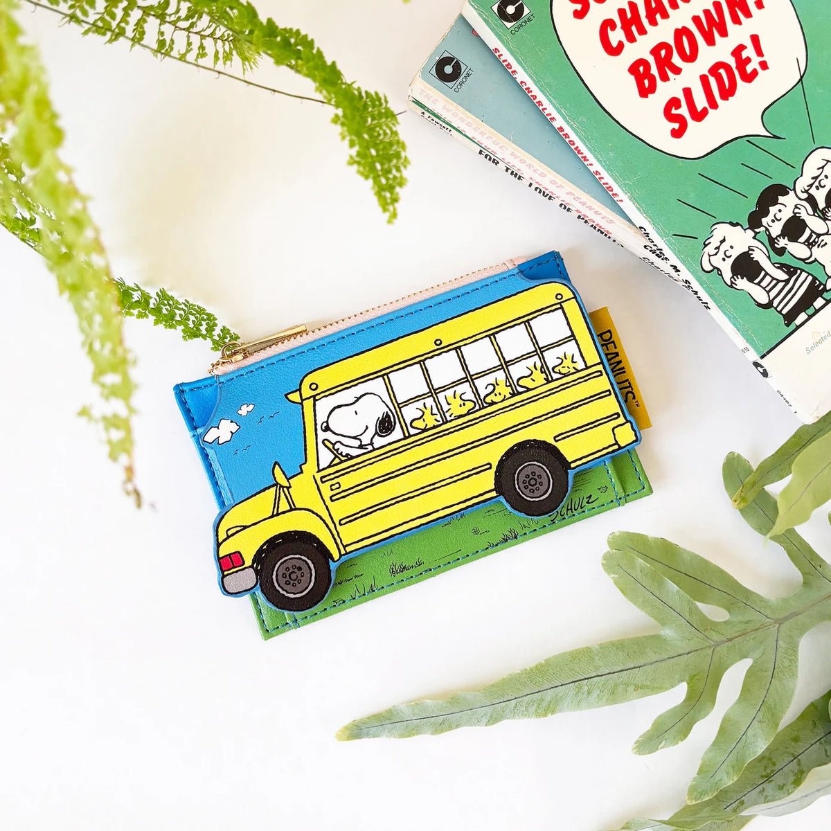 Peanuts bus purse among plants beside a Charlie Brown book