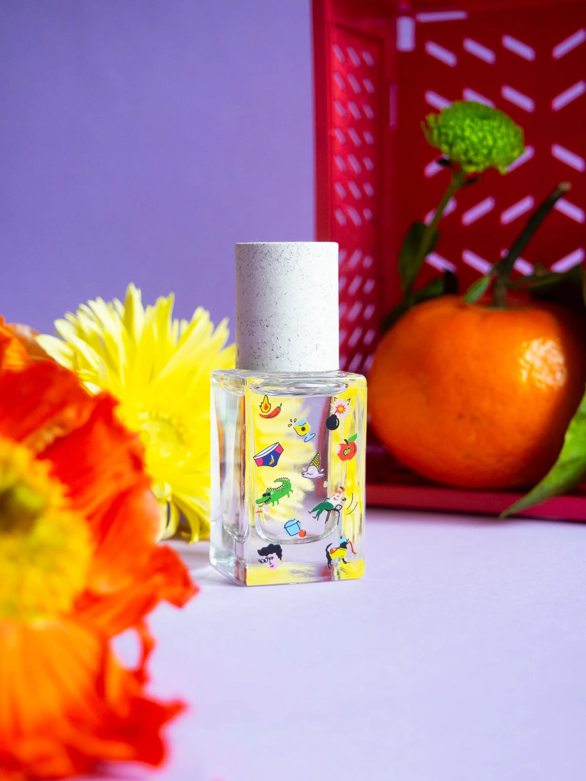 Poom Poom perfume with orange flowers and a clementine on lilac