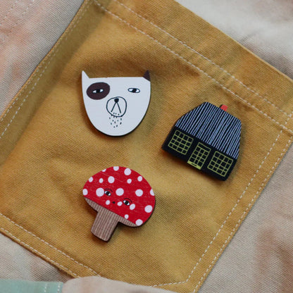 Toadie pin with a dog face pin and a house pin on a mustard cloth