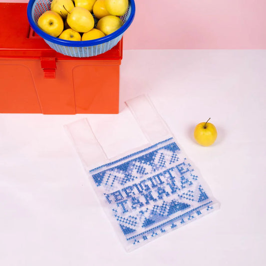 Brigitte Tanaka clear organza bag with blue cross-stitch pattern and lettering, beside a basket of lemons