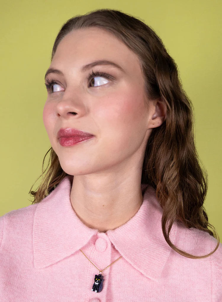Woman in a pink cardigan wearing the toy cat pendant