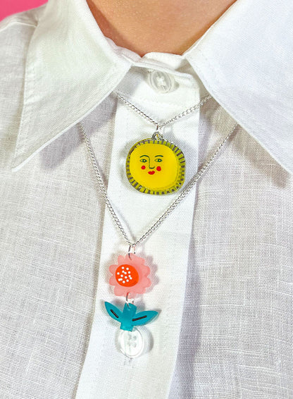 Flower pendant layered with a sun pendant on a white shirt