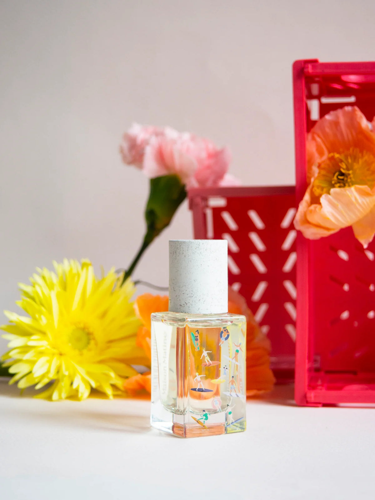 Bain de Midi perfume with pink and yellow flowers and a red crate