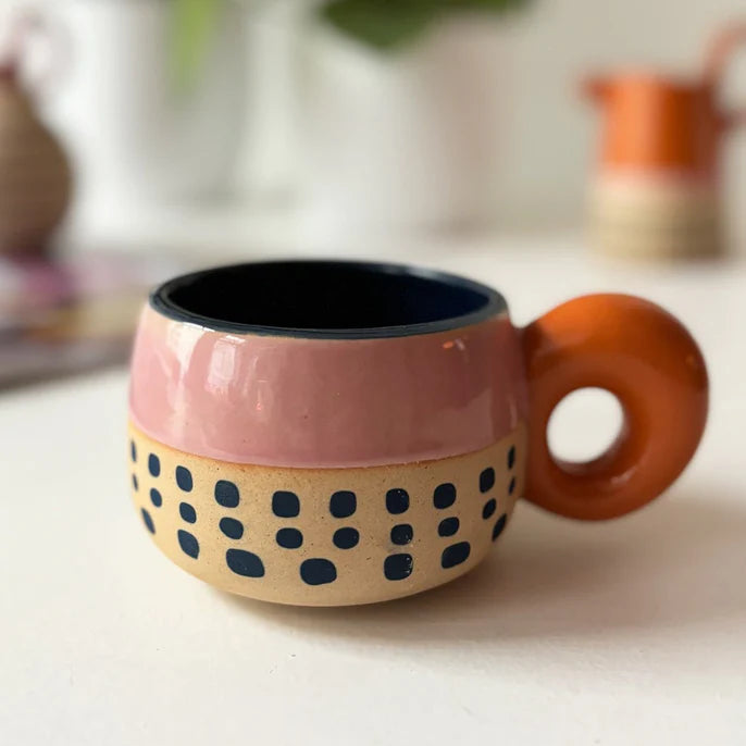 Pink and cream ceramic cup with black spots and a chunky orange ring handle