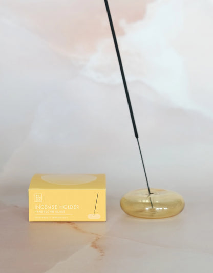 Lit incense stick in the goldenrod holder beside its box