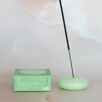 Lit incense stick in the jade green glass holder, next to its box