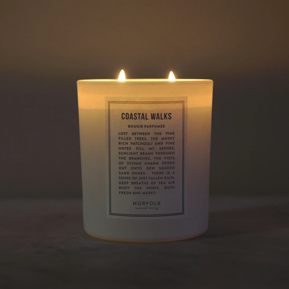Coastal Walks candle lit, with two wicks glowing in a dim room