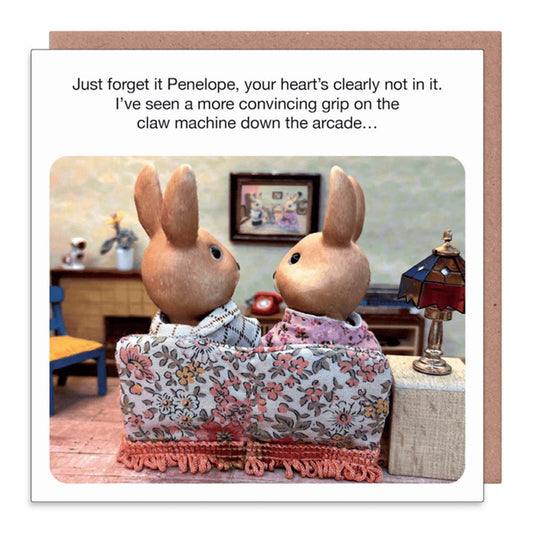 Blue Q card: two toy rabbits on a sofa, captioned 'Just forget it Penelope, your heart's clearly not in it. I've seen a more convincing grip on the claw machine down the arcade…'