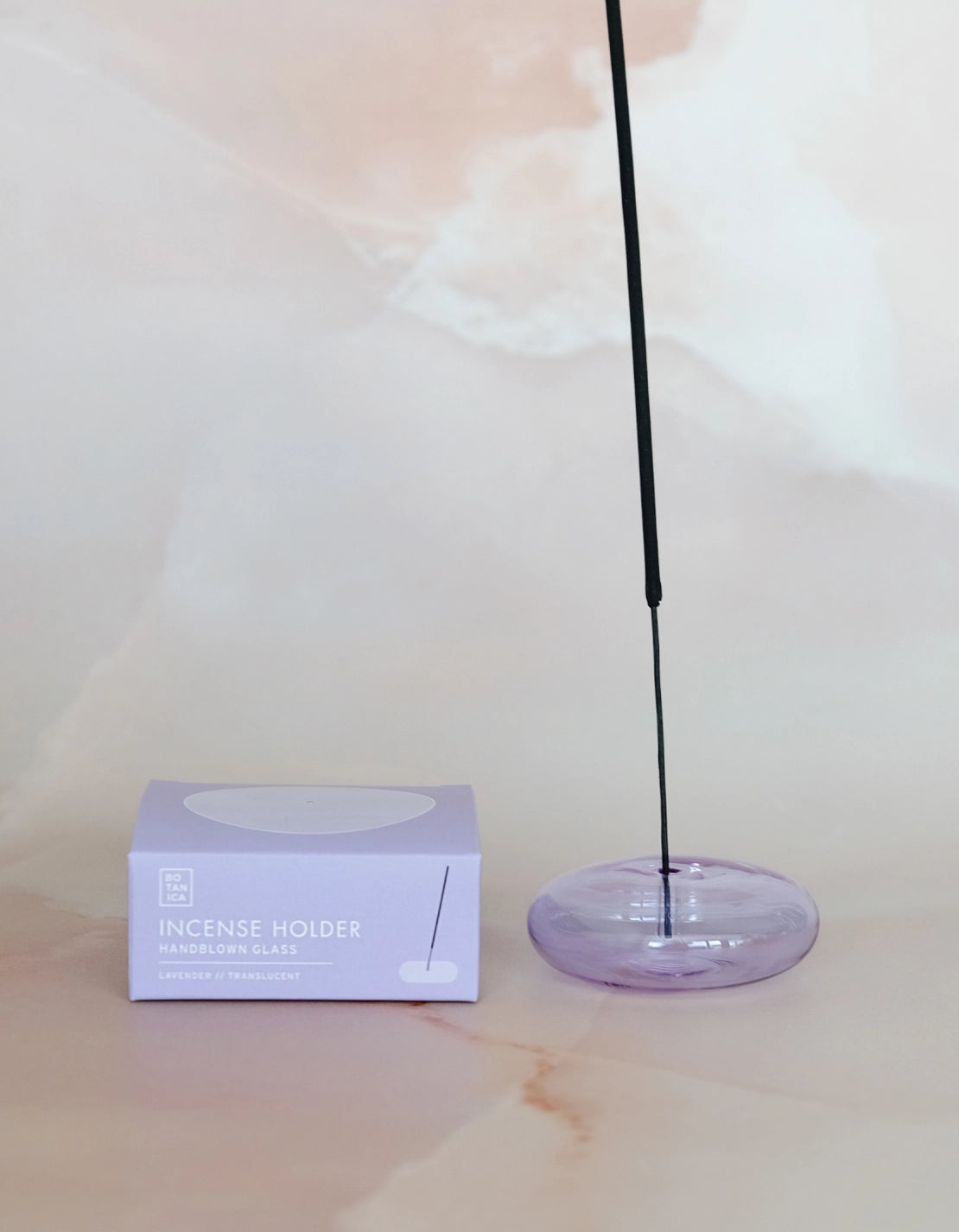 Lit incense stick in the lavender glass holder, next to its box