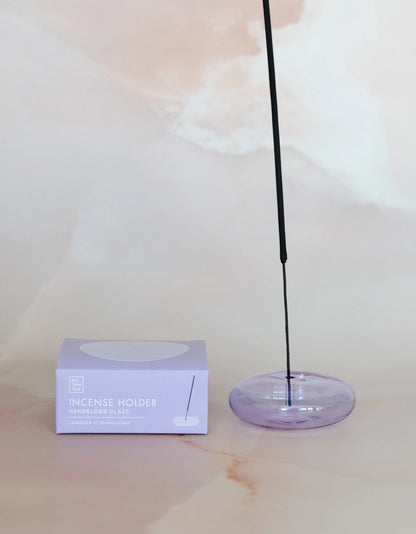 Lit incense stick in the lavender glass holder, next to its box