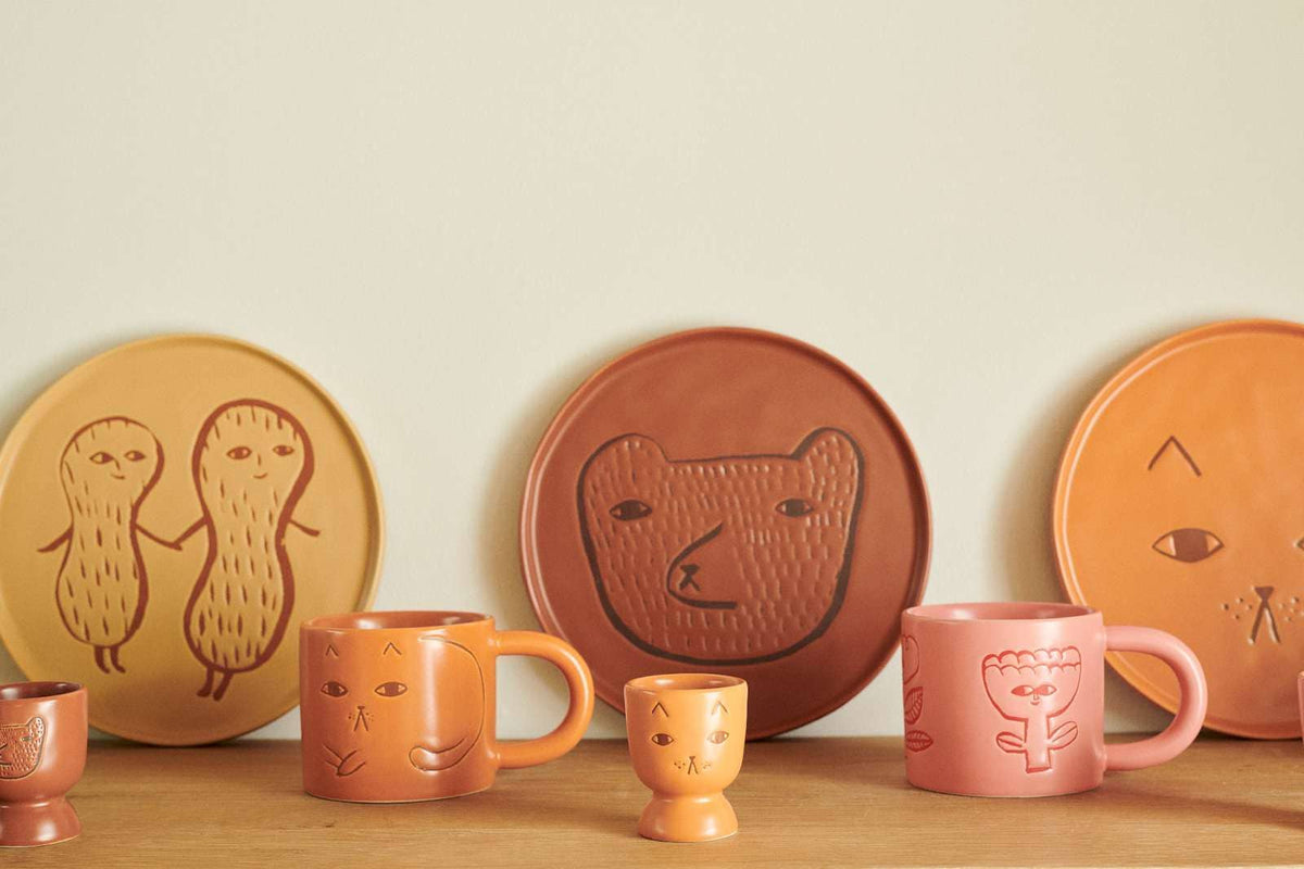 Ginger cat egg cup with Donna Wilson face plates and mugs on a shelf
