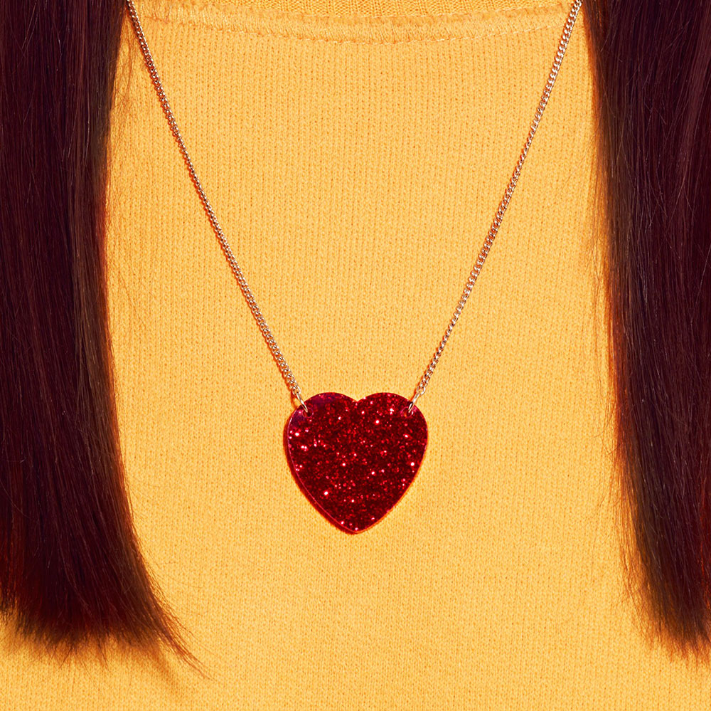 Red glitter heart necklace worn with a yellow jumper