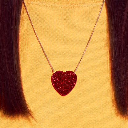Red glitter heart necklace worn with a yellow jumper