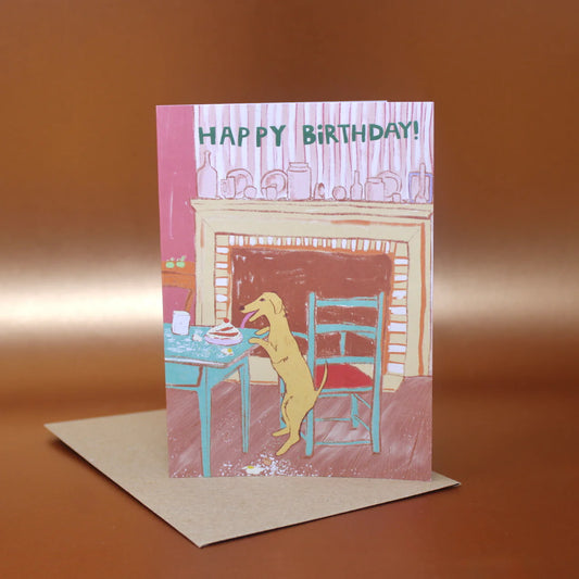 Ark card: a dog standing at a table by a fireplace, with 'Happy birthday!'