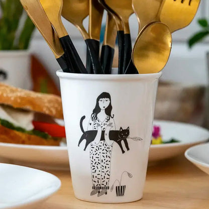 Black cat cup holding gold cutlery on a table