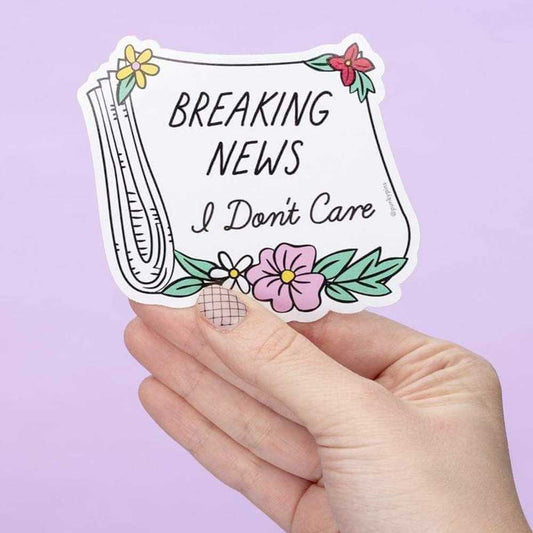 Hand holding a newspaper sticker with flowers: Breaking news, I don't care