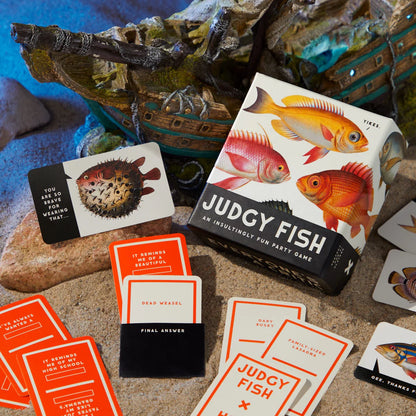 Judgy Fish game box and orange cards spread out on sand with a pufferfish card